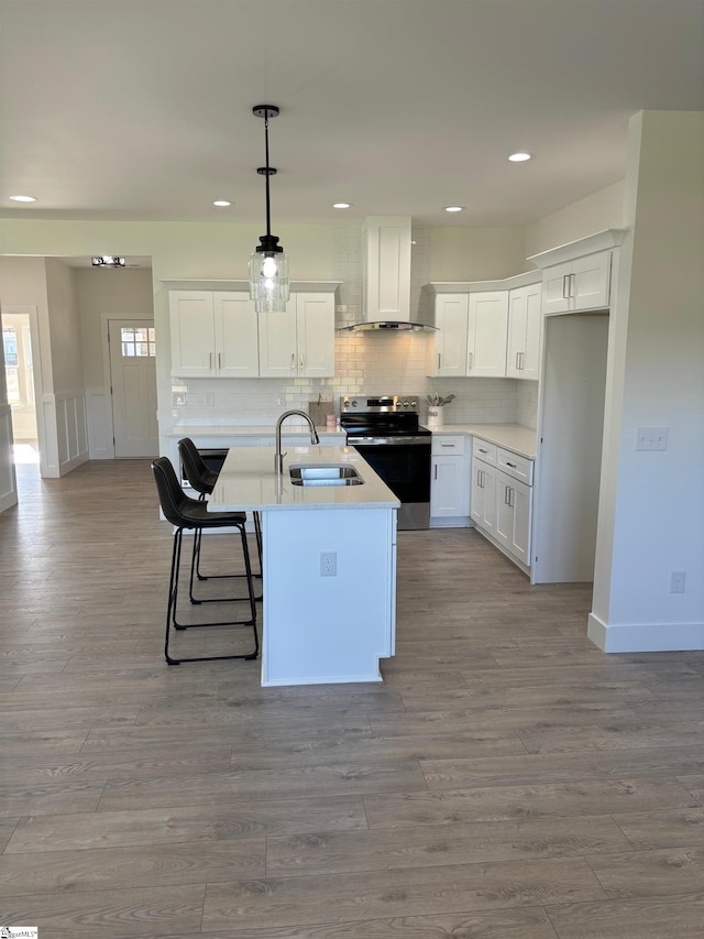 kitchen featuring wall chimney exhaust hood, sink, white cabinetry, electric range, and a kitchen island with sink