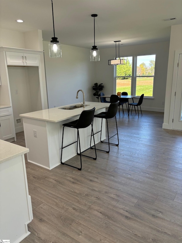 kitchen with sink, white cabinets, a center island with sink, decorative light fixtures, and light wood-type flooring