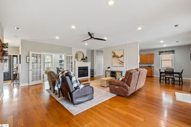 living room with a large fireplace, ceiling fan, and light hardwood / wood-style flooring