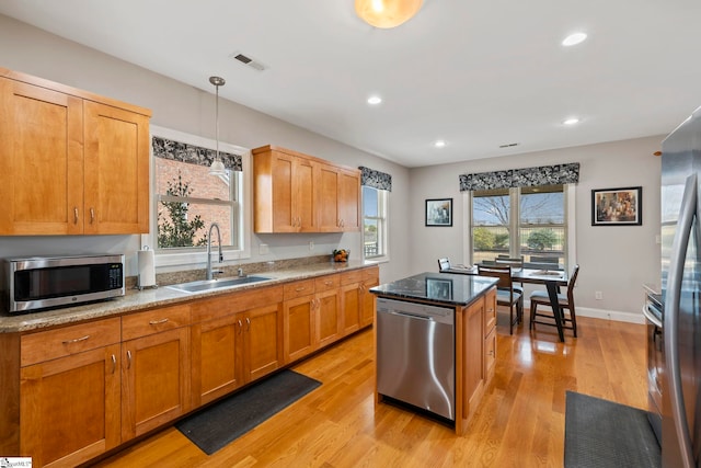 kitchen with appliances with stainless steel finishes, decorative light fixtures, sink, dark stone countertops, and light wood-type flooring