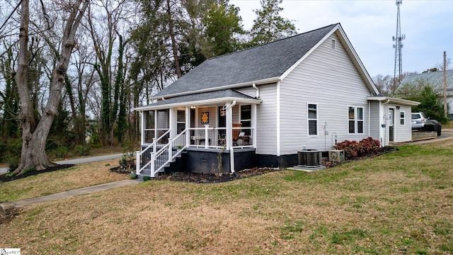 view of front of home featuring central air condition unit, covered porch, a shingled roof, and a front lawn