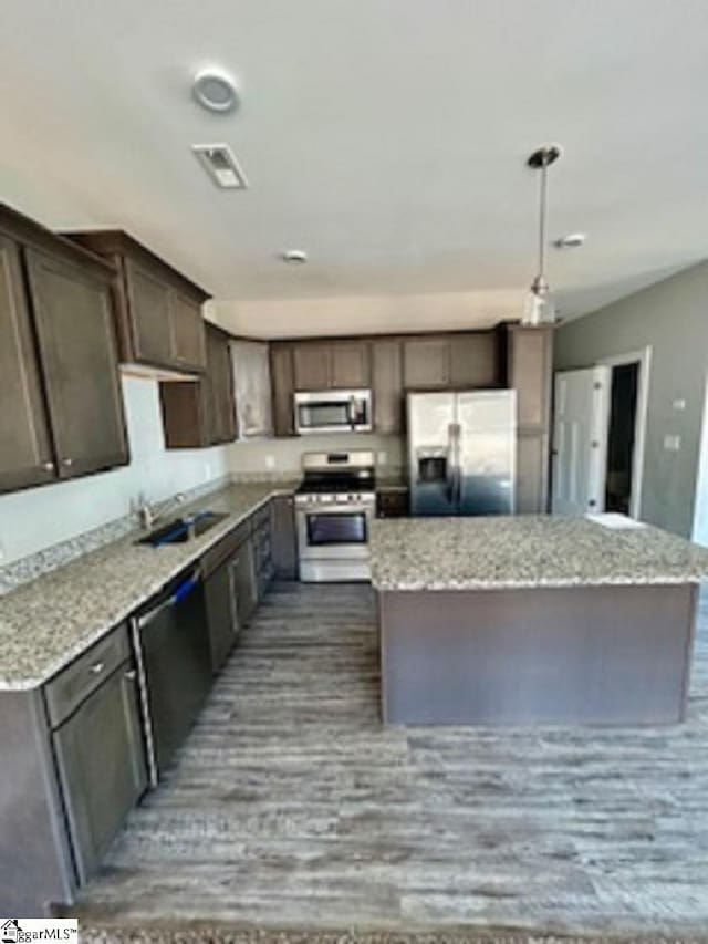 kitchen with a center island, appliances with stainless steel finishes, sink, and light stone counters