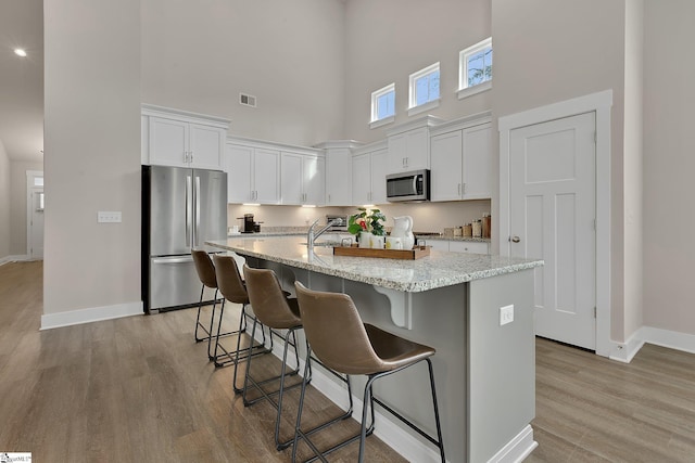 kitchen with appliances with stainless steel finishes, light stone countertops, a center island with sink, and white cabinets