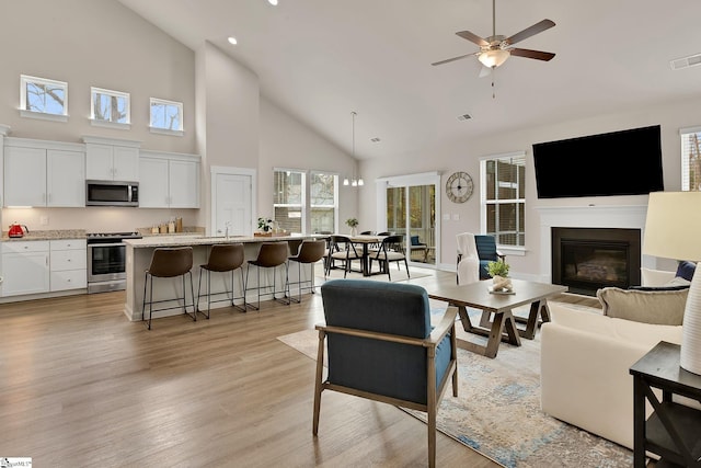 living room featuring high vaulted ceiling, light hardwood / wood-style floors, and ceiling fan