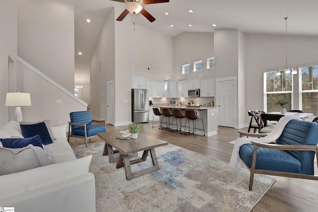 living room with lofted ceiling, ceiling fan with notable chandelier, and light hardwood / wood-style floors