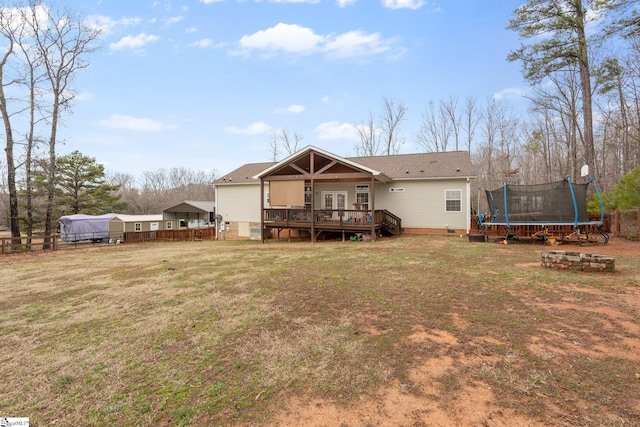 rear view of property featuring a trampoline, a wooden deck, and a lawn