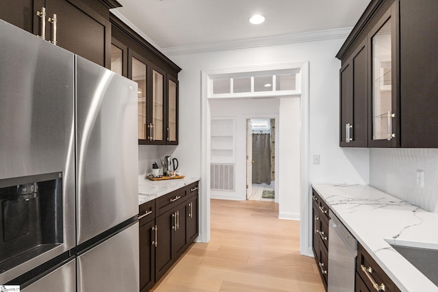 kitchen with ornamental molding, stainless steel appliances, light stone countertops, and light hardwood / wood-style flooring