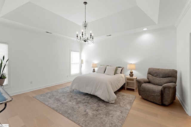 bedroom with an inviting chandelier, ornamental molding, a tray ceiling, and light hardwood / wood-style floors