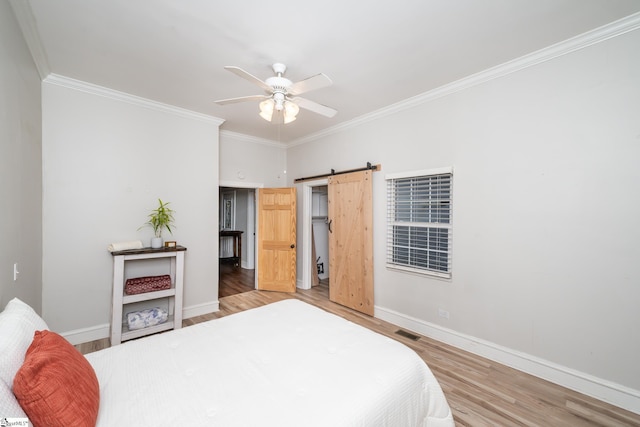 bedroom featuring ceiling fan, ornamental molding, a barn door, and hardwood / wood-style floors