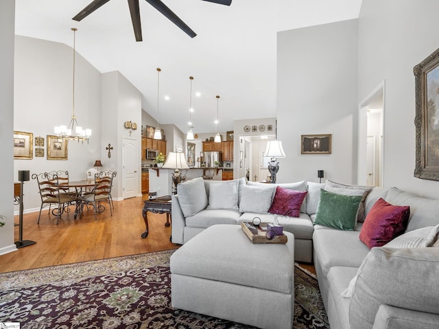 living room featuring hardwood / wood-style floors, ceiling fan with notable chandelier, and high vaulted ceiling