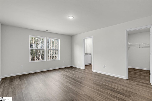 unfurnished bedroom featuring dark wood-type flooring, ensuite bathroom, a spacious closet, and a closet