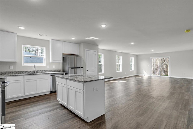 kitchen featuring white cabinetry, wood-type flooring, a center island, appliances with stainless steel finishes, and light stone countertops