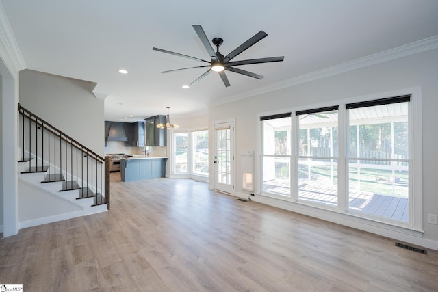 unfurnished living room featuring ornamental molding, ceiling fan with notable chandelier, and light wood-type flooring