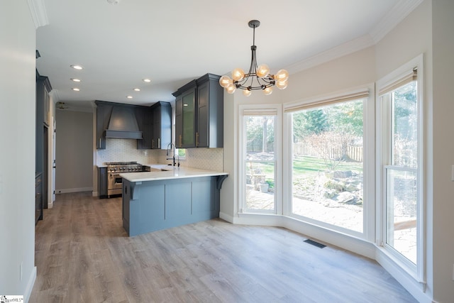 kitchen with high end range, hanging light fixtures, tasteful backsplash, custom exhaust hood, and kitchen peninsula