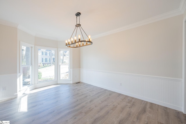 unfurnished room with a notable chandelier, ornamental molding, and light wood-type flooring