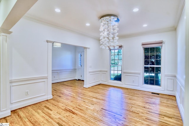 unfurnished dining area featuring an inviting chandelier, ornamental molding, light hardwood / wood-style flooring, and ornate columns