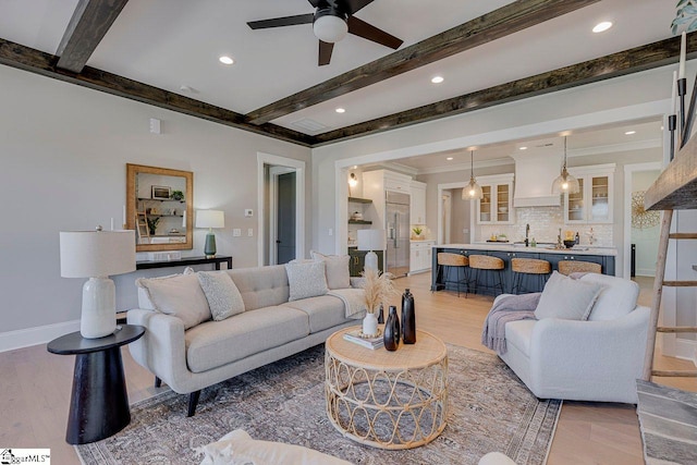 living room featuring ceiling fan, crown molding, light hardwood / wood-style floors, and beamed ceiling