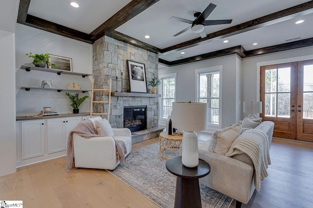 living room featuring a stone fireplace, light hardwood / wood-style flooring, french doors, and beamed ceiling