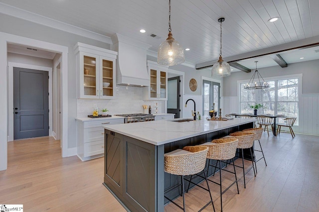 kitchen with pendant lighting, white cabinetry, a spacious island, light stone counters, and custom exhaust hood