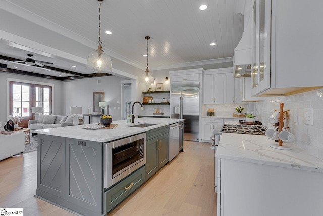 kitchen featuring decorative light fixtures, sink, a kitchen island with sink, built in appliances, and light hardwood / wood-style flooring