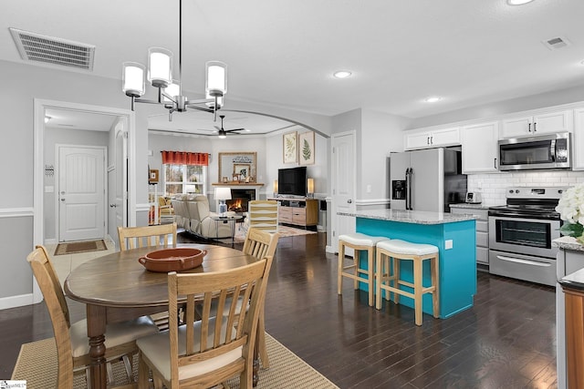 dining space with dark wood-type flooring and ceiling fan with notable chandelier