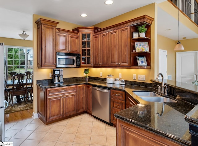 kitchen featuring sink, light tile patterned floors, appliances with stainless steel finishes, decorative light fixtures, and dark stone counters