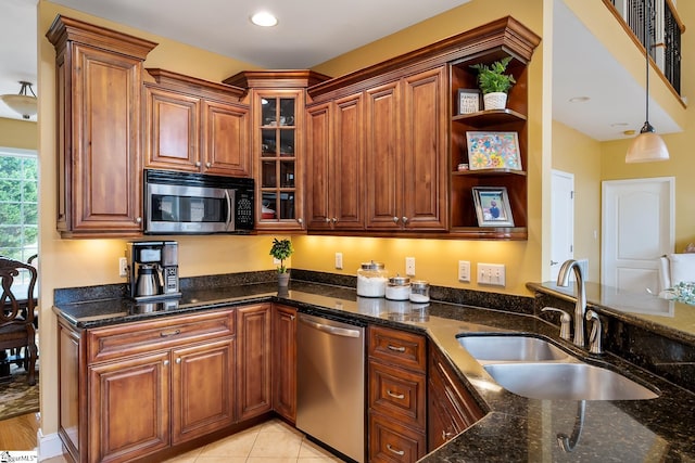 kitchen with pendant lighting, sink, stainless steel appliances, light tile patterned flooring, and dark stone counters