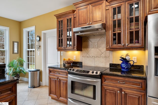 kitchen featuring tasteful backsplash, dark stone countertops, light tile patterned floors, stainless steel appliances, and plenty of natural light