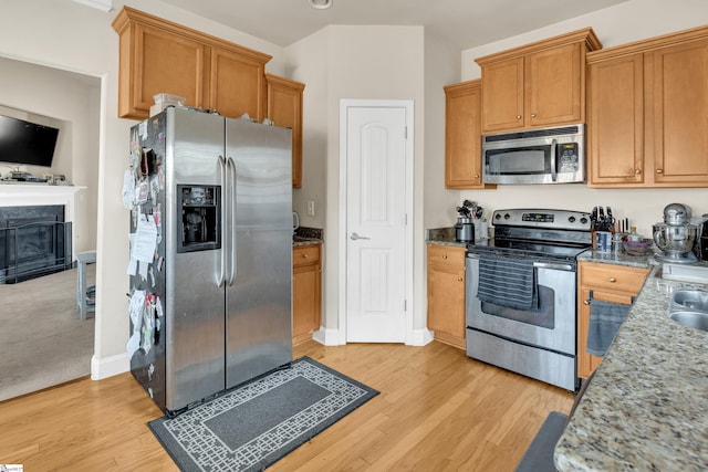 kitchen with stainless steel appliances, light stone countertops, and light hardwood / wood-style floors