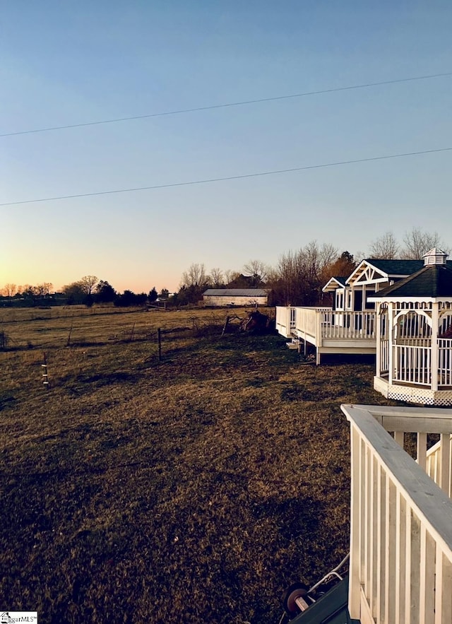 yard at dusk with a rural view, a gazebo, and a deck