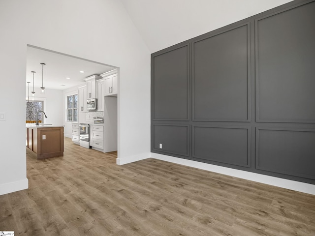 unfurnished living room with lofted ceiling, sink, and light hardwood / wood-style floors