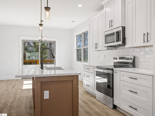 kitchen featuring sink, decorative light fixtures, an island with sink, stainless steel appliances, and white cabinets