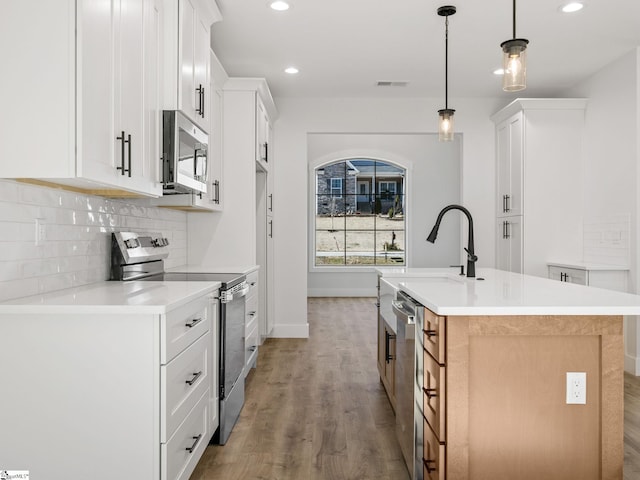 kitchen with white cabinetry, appliances with stainless steel finishes, a kitchen island with sink, and pendant lighting