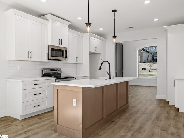 kitchen featuring decorative light fixtures, white cabinets, stainless steel appliances, a center island with sink, and light wood-type flooring