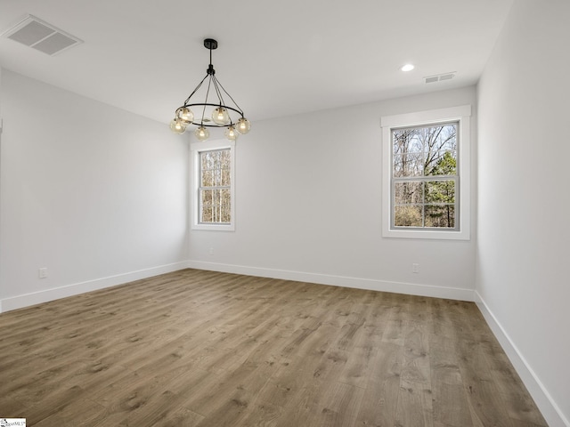 empty room with hardwood / wood-style flooring and a notable chandelier