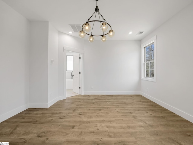 empty room featuring wood-type flooring and a notable chandelier