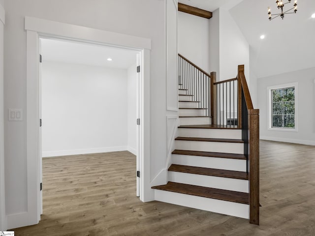 stairway with wood-type flooring, high vaulted ceiling, and a chandelier