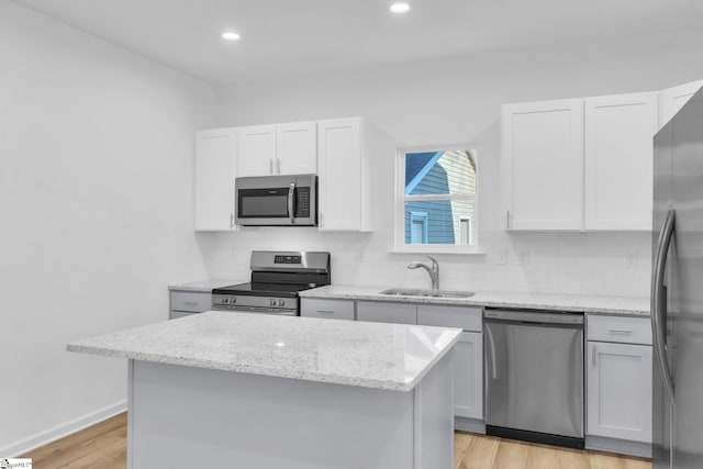 kitchen featuring sink, white cabinetry, stainless steel appliances, light stone counters, and a kitchen island