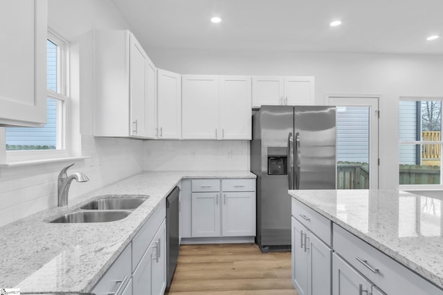 kitchen featuring sink, backsplash, stainless steel appliances, a wealth of natural light, and light stone countertops