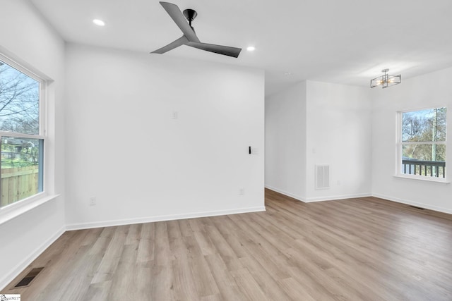 empty room with ceiling fan with notable chandelier, a healthy amount of sunlight, and light hardwood / wood-style floors