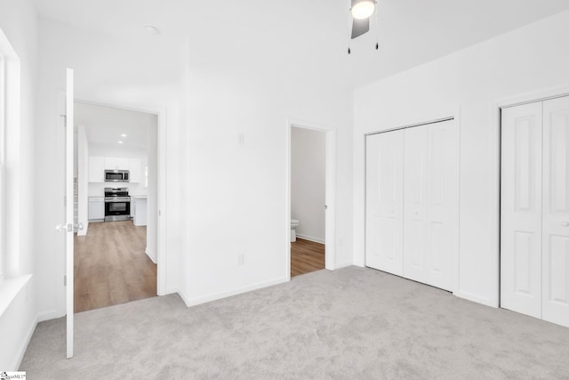 unfurnished bedroom featuring ceiling fan, ensuite bath, light colored carpet, and multiple closets