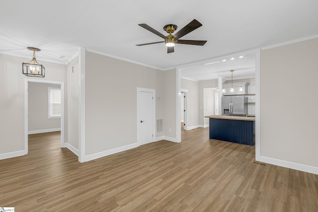 unfurnished living room with hardwood / wood-style flooring, ornamental molding, and ceiling fan with notable chandelier