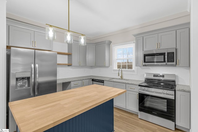 kitchen featuring light stone counters, sink, stainless steel appliances, and hanging light fixtures