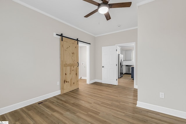 spare room featuring ornamental molding, a barn door, ceiling fan, and light wood-type flooring