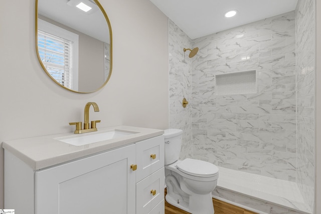 bathroom featuring vanity, wood-type flooring, a tile shower, and toilet