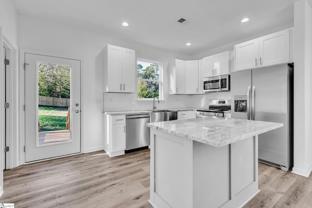 kitchen featuring white cabinetry, backsplash, a center island, light stone counters, and stainless steel appliances