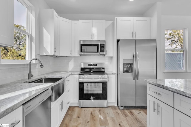 kitchen with light hardwood / wood-style flooring, appliances with stainless steel finishes, white cabinets, light stone countertops, and backsplash