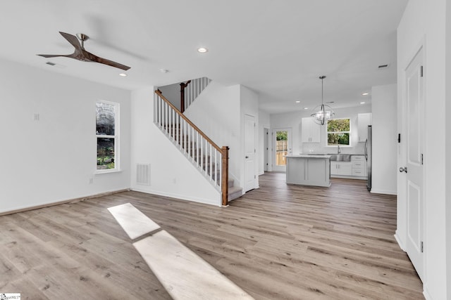 unfurnished living room with ceiling fan with notable chandelier, sink, and light hardwood / wood-style floors