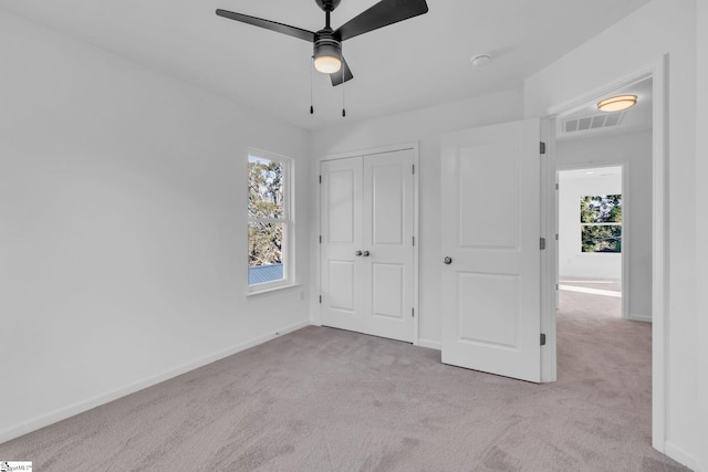 unfurnished bedroom featuring multiple windows, light colored carpet, ceiling fan, and a closet