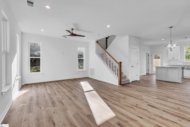 unfurnished living room featuring ceiling fan with notable chandelier and light hardwood / wood-style flooring